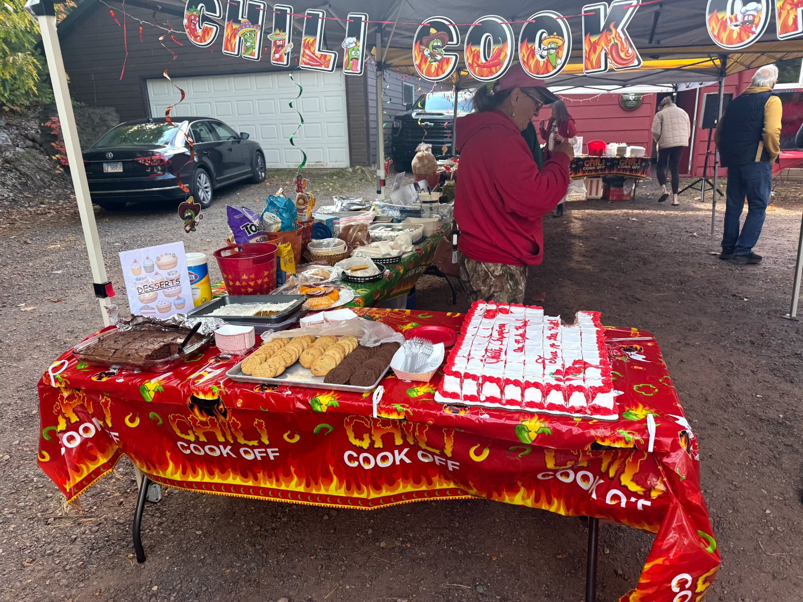 A table covered in a flame-print cloth with food, under a Chili Cook Off banner.