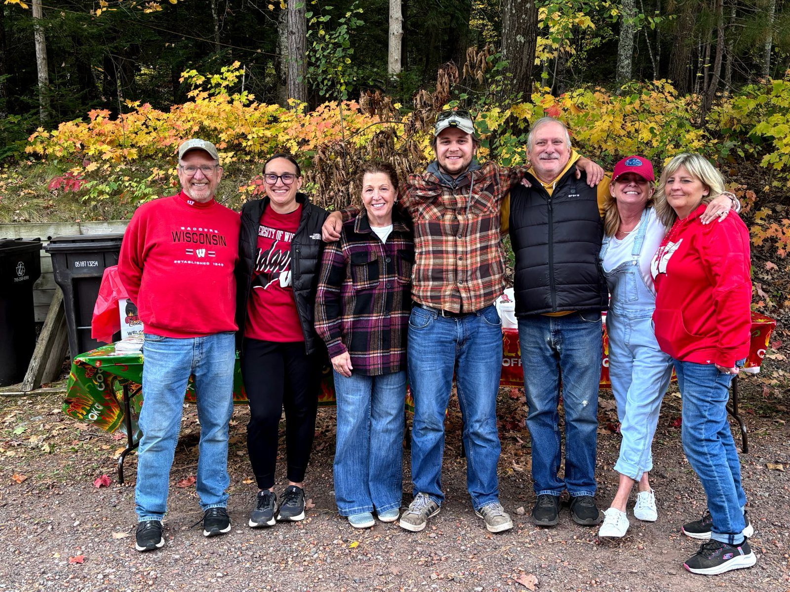 Seven people stand together for a photo in front of fall trees.